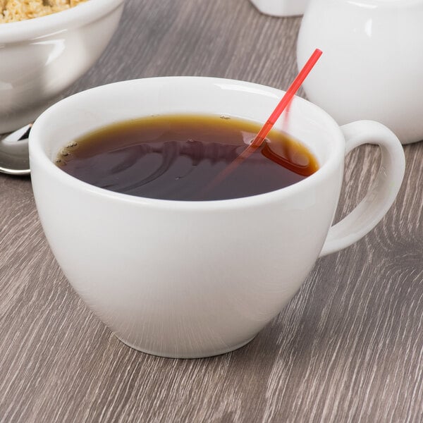 A Libbey ivory porcelain coffee cup with a straw in it filled with brown liquid.