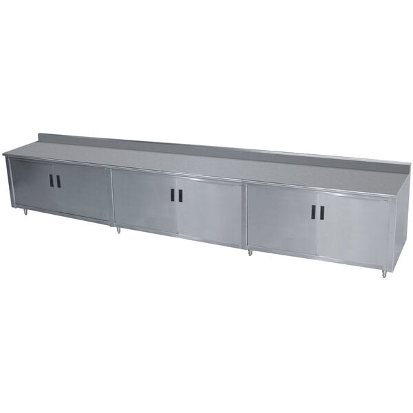 A stainless steel Advance Tabco enclosed base work table with hinged doors and drawers.