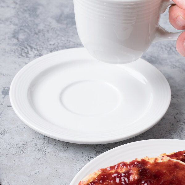 A hand holding a white Libbey Aluma Stacking Saucer under a white cup of coffee.