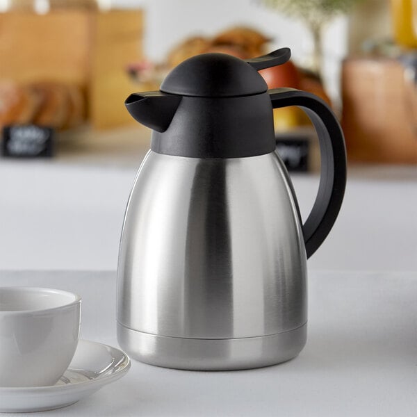 Insulated thermal coffee carafe sitting next to coffee cup