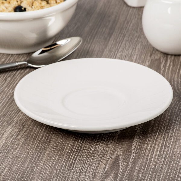 A Libbey ivory porcelain medium saucer with a spoon on a table.