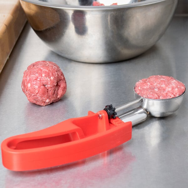 A Vollrath red ice cream scoop with a metal bowl filled with meatballs.