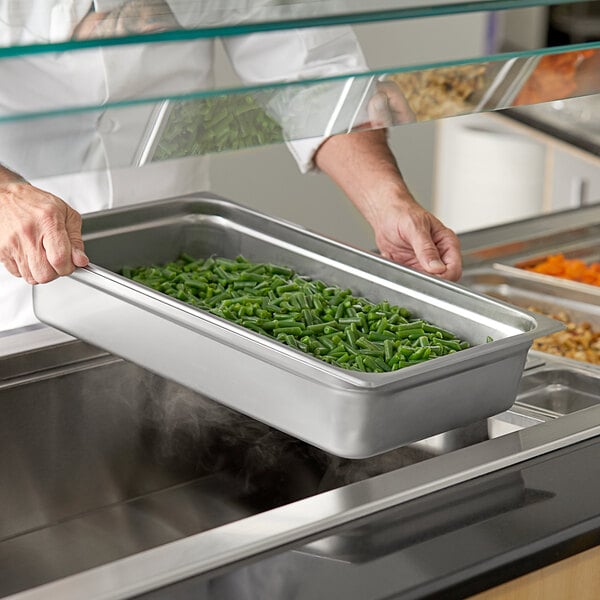 A person in a white coat putting food into a Choice stainless steel steam table pan.