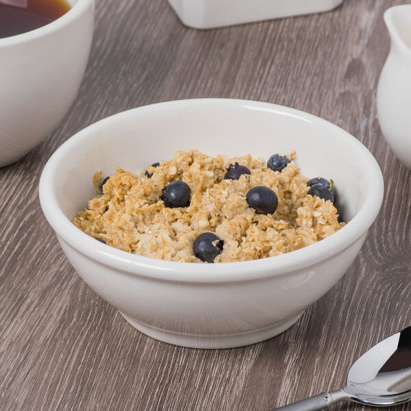 A Libbey ivory porcelain bowl filled with oatmeal, blueberries, and a spoon.