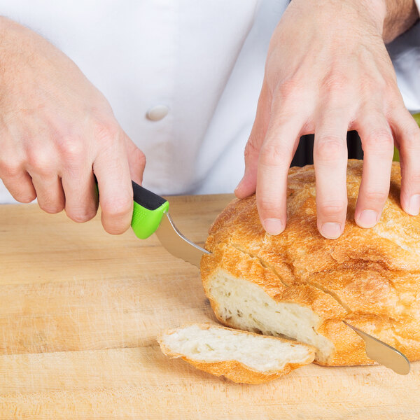 A person cutting a loaf of bread with a Mercer Culinary bread knife with a green handle.