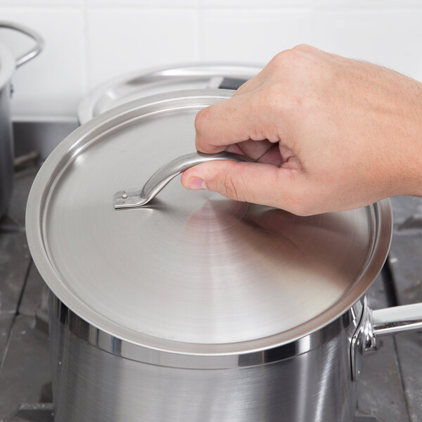 A hand using a Vollrath stainless steel domed cover on a pot.