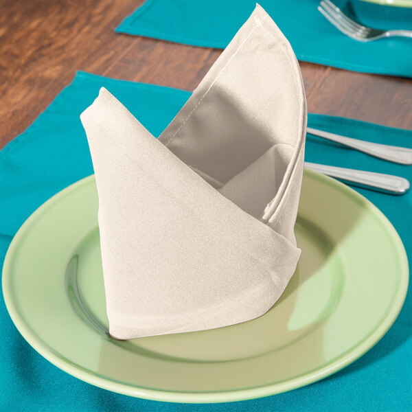 A folded ivory Intedge cloth napkin on a plate with silverware.