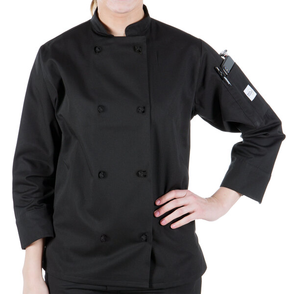 A woman wearing a Mercer Culinary black long sleeve chef coat with cloth knot buttons.