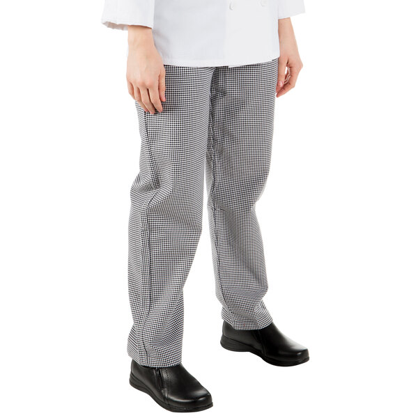 A woman wearing Mercer Culinary black and white houndstooth chef pants with a hand in the pocket.