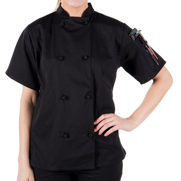 A woman wearing a Mercer Culinary black chef coat with cloth knot buttons.