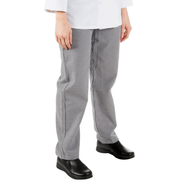 A woman wearing Mercer Culinary Genesis houndstooth chef pants with a hand in the pocket.