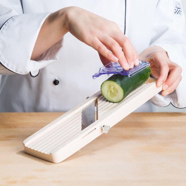A person using a Benriner Little Beni Japanese mandoline to slice a cucumber.