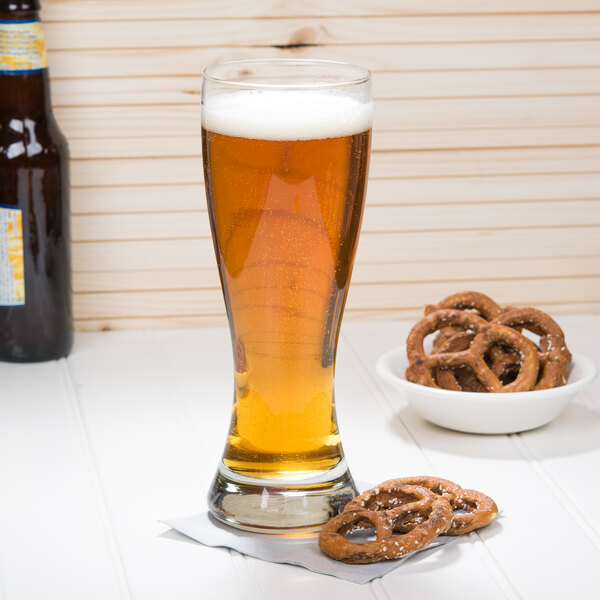 A close up of an Anchor Hocking Pilsner glass of beer with pretzels.