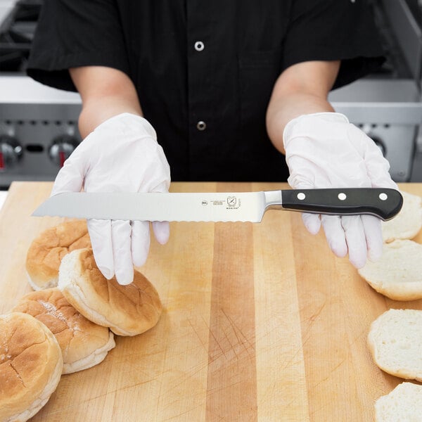 A person in gloves using a Mercer Culinary bread knife to cut a bun.
