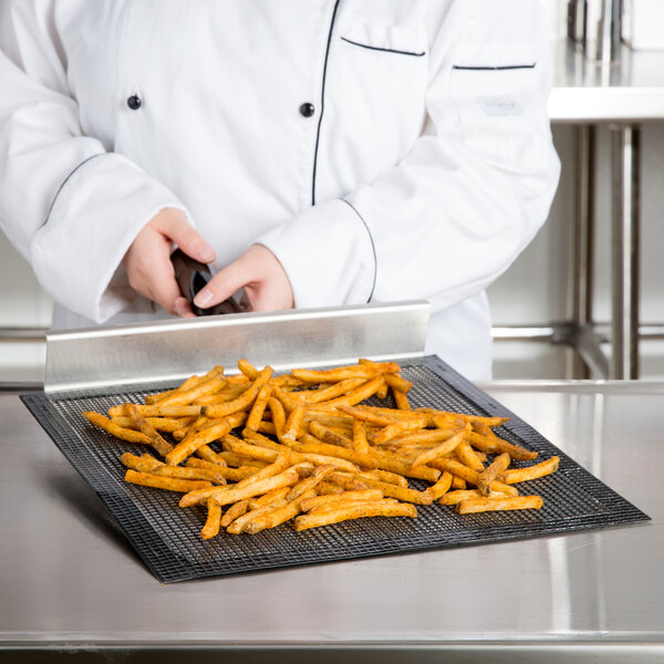 A chef cutting french fries on a Baker's Mark black mesh screen.