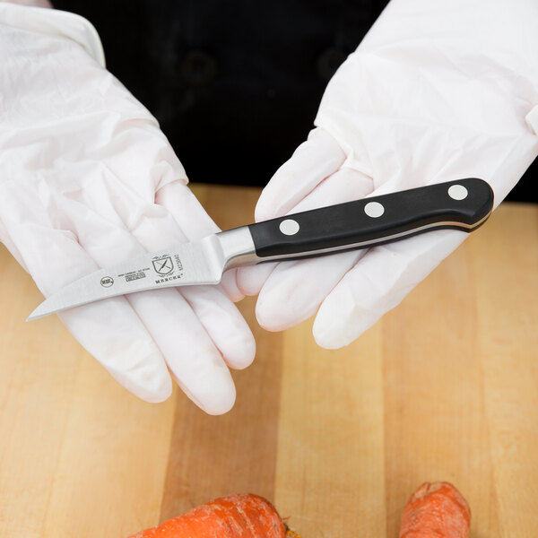 A person in white gloves using a Mercer Culinary Renaissance peeling knife to peel an orange.