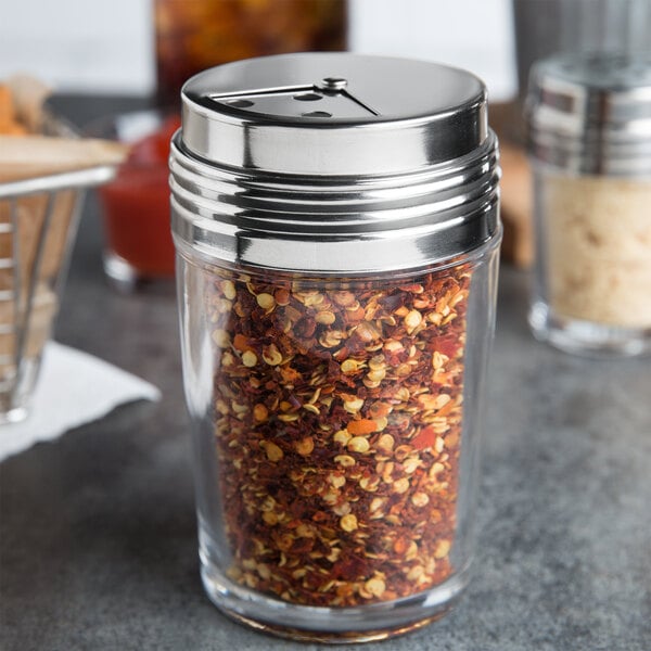 An American Metalcraft clear glass shaker with a stainless steel top filled with red pepper flakes.