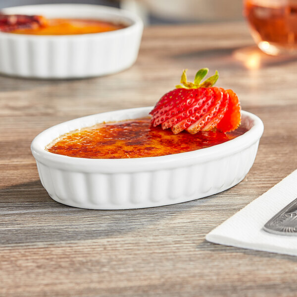 An Acopa fluted white porcelain dish filled with creme brulee and strawberries with a spoon.