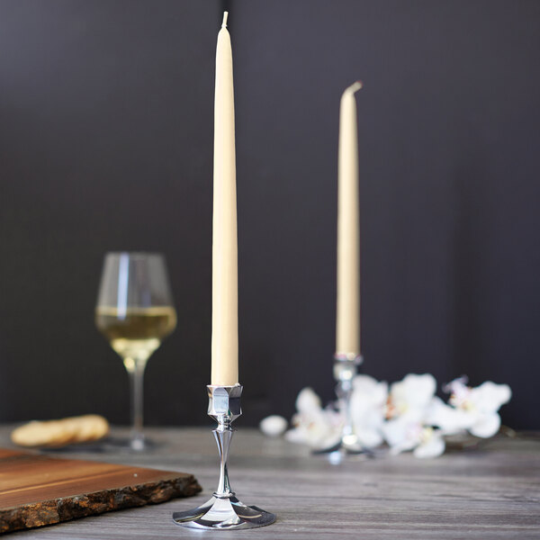 Two ivory Sterno 12" taper candles on a wooden table with a glass of wine.