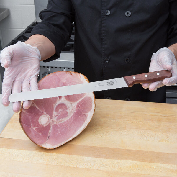A person using a Victorinox rosewood carving knife to slice ham.
