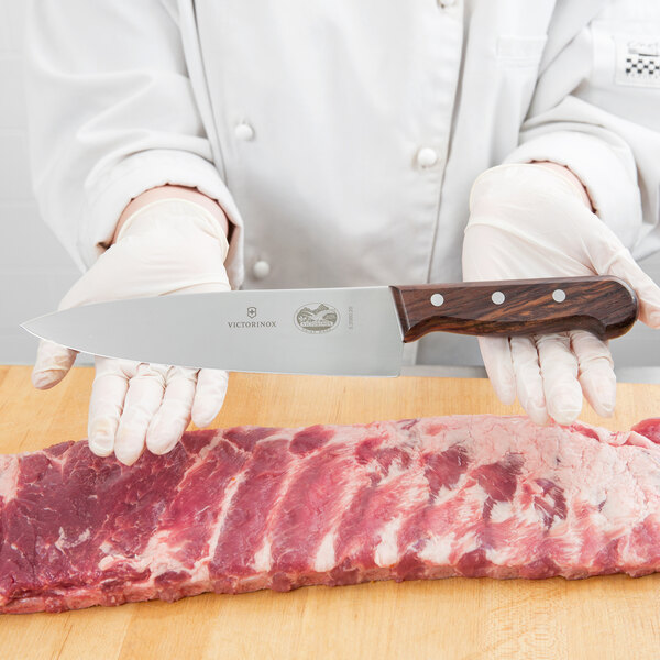 A chef holding a Victorinox 8" Chef Knife over a piece of meat on a wooden surface.
