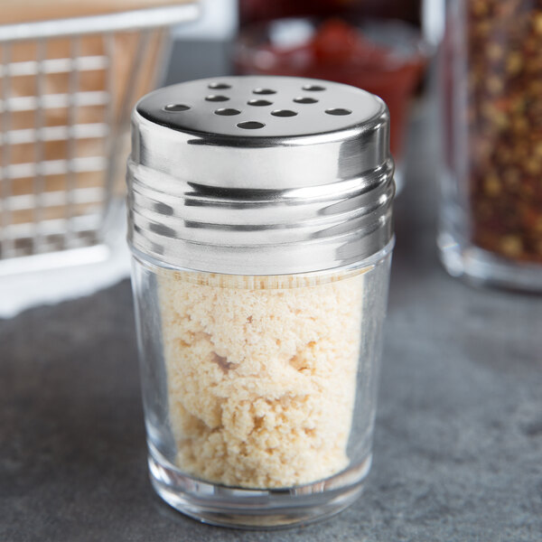 An American Metalcraft clear glass cheese shaker with a stainless steel top filled with salt.