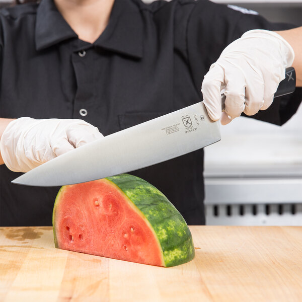 A person holding a Mercer Culinary chef knife and cutting a watermelon.