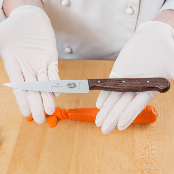 A person in white gloves using a Victorinox serrated utility knife to cut a carrot.