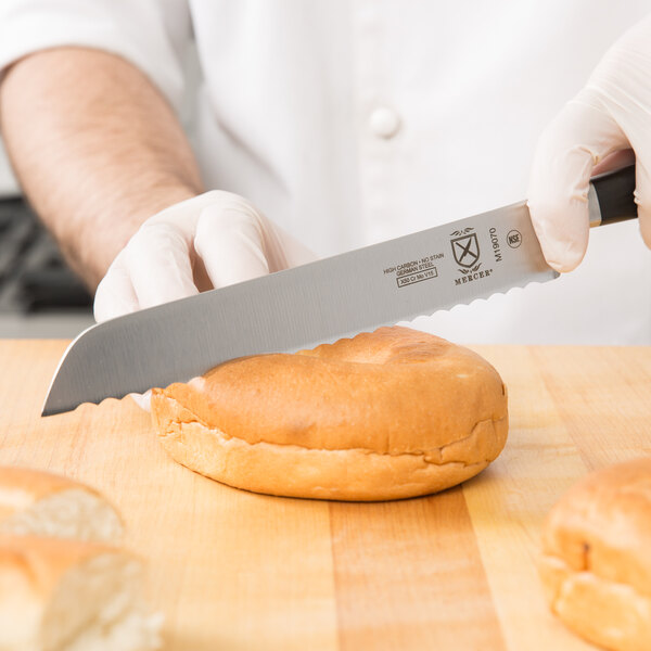 A person using a Mercer Culinary Z&#252;M bread knife to cut a baguette.
