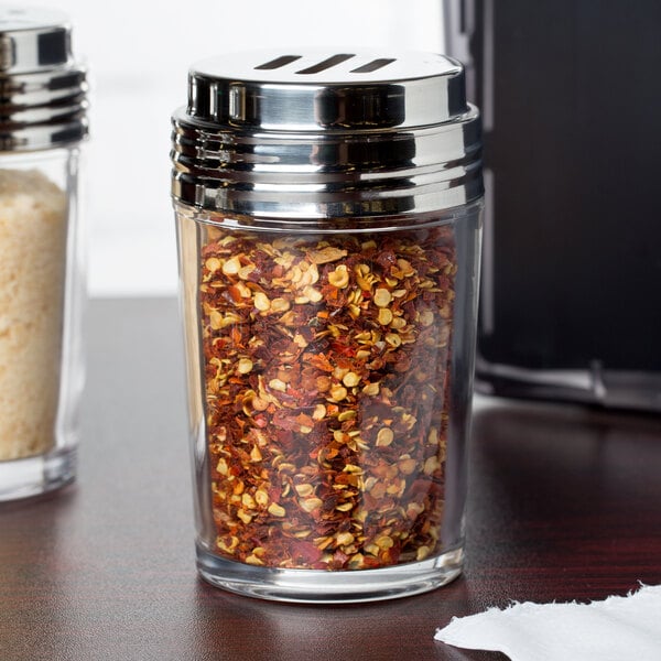 An American Metalcraft clear glass spice shaker with red and yellow flakes inside.