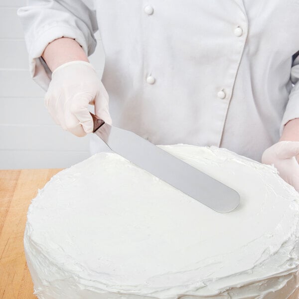 A person in a white coat using a Victorinox baking spatula to cut a cake.