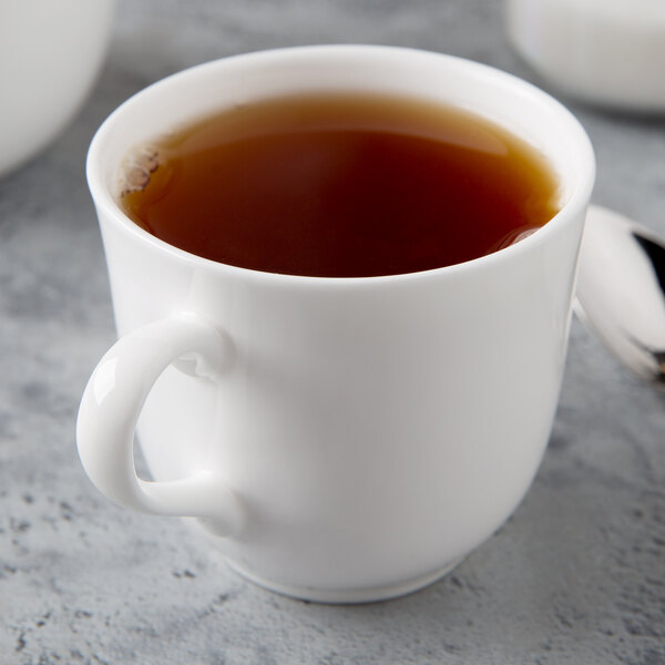A close up of a Reserve by Libbey Bone China tea cup filled with tea next to a spoon.