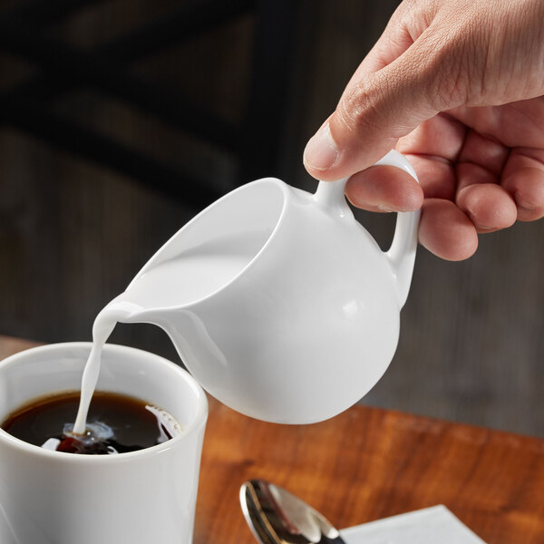 A person pouring milk into a white Reserve by Libbey bone china creamer.