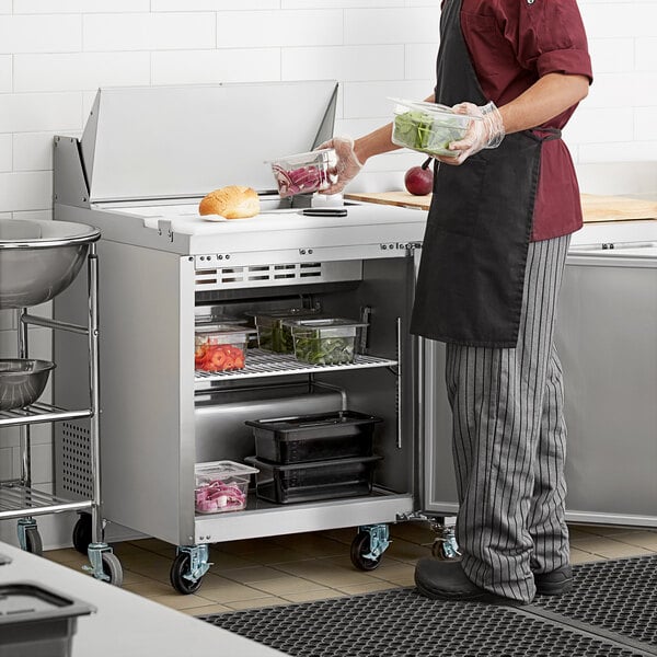 A man in a chef's uniform using an Avantco stainless steel refrigerated sandwich prep table.