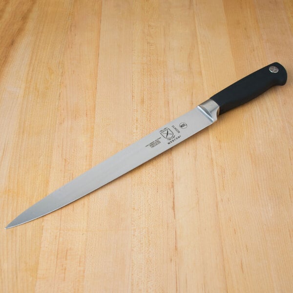 A Mercer Culinary Genesis Forged Carving Knife with a black handle on a wooden table.