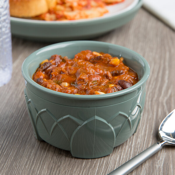 A bowl of Dinex Fenwick Sage insulated dinnerware filled with chili on a table with a spoon.