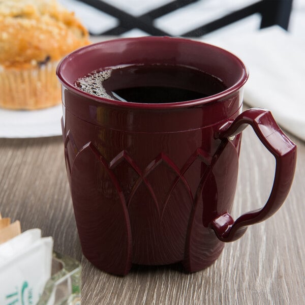 A red Dinex insulated mug filled with a drink sits on a table next to muffins.