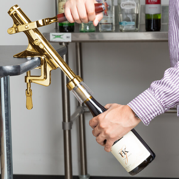 A person using a Franmara brass-plated wine bottle opener to open a bottle of wine.