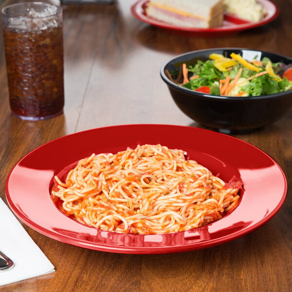 A red Diamond Harvest melamine bowl filled with spaghetti and salad on a table.
