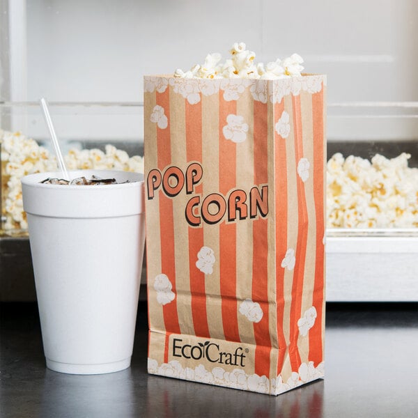 An EcoCraft popcorn bag on a table next to a cup of soda.