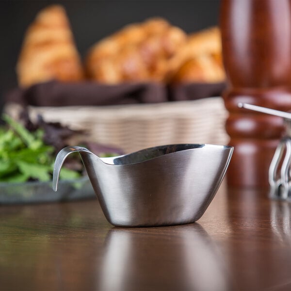 A Tablecraft stainless steel gravy boat on a table with bread.