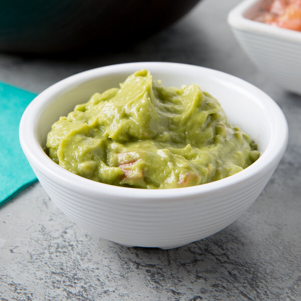 A Tablecraft white round ribbed melamine ramekin filled with guacamole on a table.