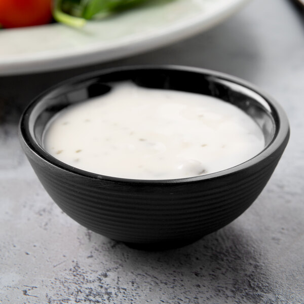 A bowl of white sauce in a Tablecraft black melamine ramekin.