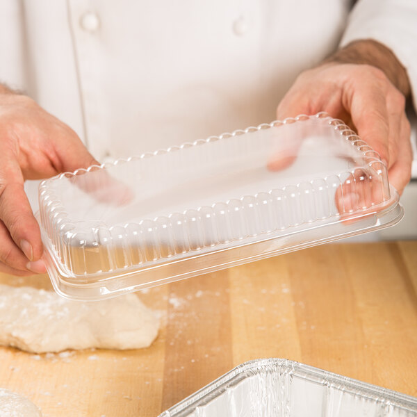 A person holding a D&W clear plastic container with a clear dome lid over dough.