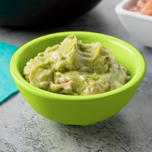 A green Tablecraft round ribbed melamine ramekin filled with guacamole on a table with a bowl of chips.