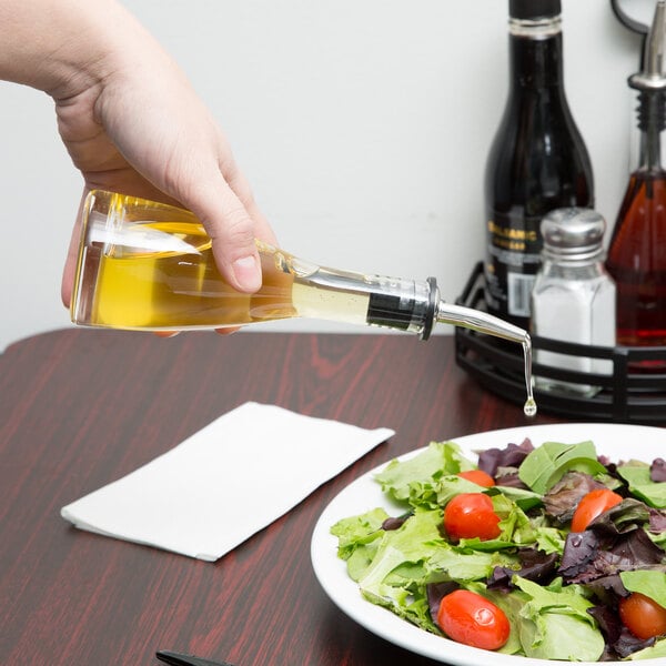 A hand pouring oil from a Tablecraft Siena oil and vinegar bottle onto a salad.