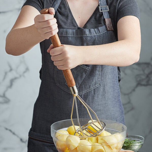 A person using a Thunder Group chrome plated potato masher to mash potatoes in a bowl.