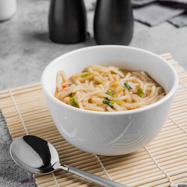 A bowl of noodles with vegetables and a spoon in a Libbey bright white porcelain bowl.