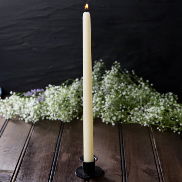 A Hyoola ivory taper candle in a white candle holder on a table.