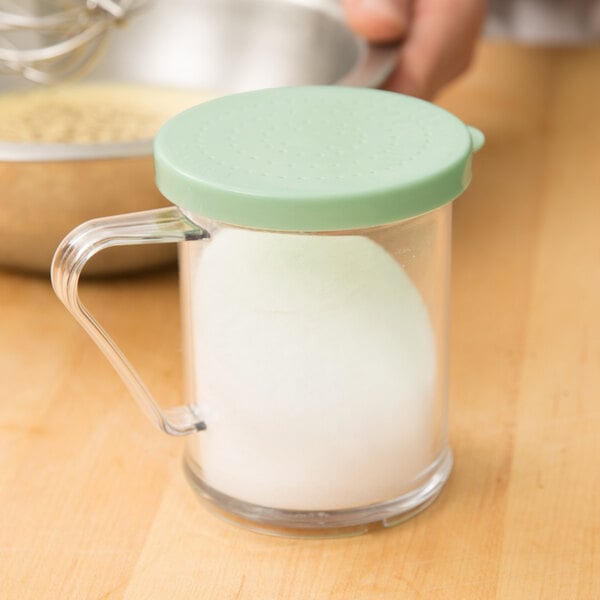 A glass Cambro shaker with a green lid filled with white sugar.